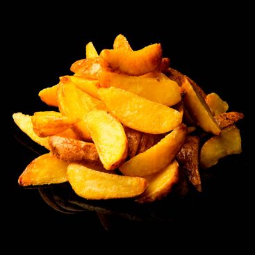 Golden fried potato wedges piled on a black reflective surface