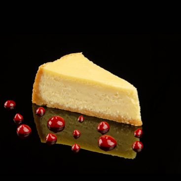Slice of classic cheesecake with drops of berry sauce, shot from the side