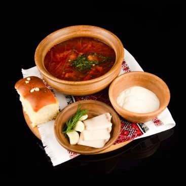 Ukrainian borscht in a clay bowl with sour cream, garlic bun and sliced salo, on an embroidered towel