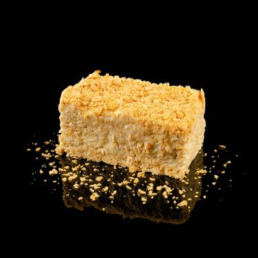 Slice of Napoleon cake with custard cream layers and puff pastry crumbs, on a black reflective surface