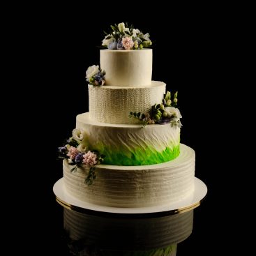 Four-tier white wedding cake with fresh flowers and a green ombré tier, on a black background