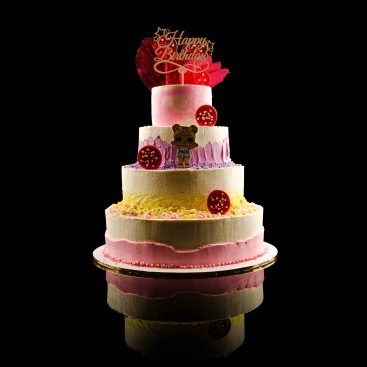 Four-tier pink and white birthday cake with Happy Birthday topper, doll figure and sprinkles